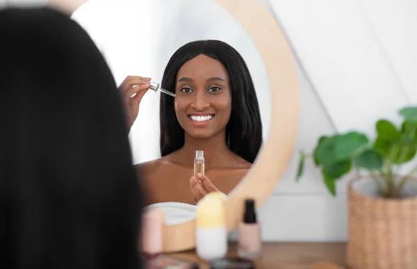 Cosmetología y spa. Sonriente milenaria africana americana dama mantenga pipeta con aceite cosmético — Foto de Stock