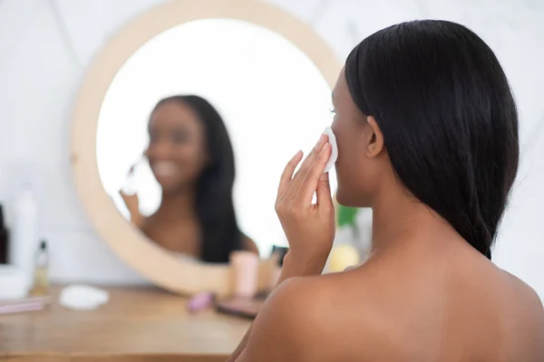 Makeupborttagning, återfuktning och kosmetika. Leende ung afrikansk amerikansk kvinna tittar i spegeln — Stockfoto