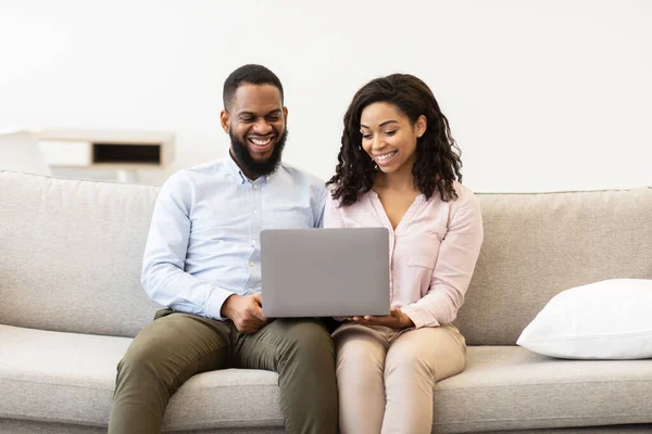 Africano casal americano sentado no sofá, usando computador portátil — Fotografia de Stock