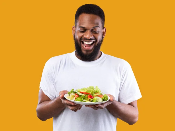 Homem Africano excitado segurando placa de salada em pé sobre fundo amarelo — Fotografia de Stock