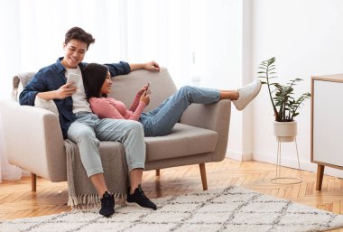 Çinli çift telefonlarını kullanarak evdeki koltukta dinleniyor.
