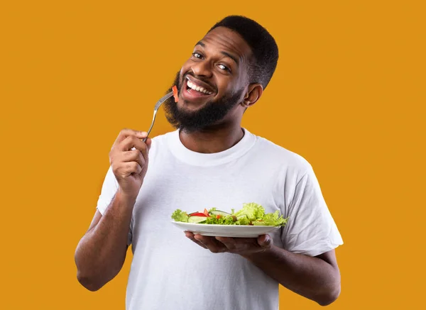 Alegre preto cara comer salada desfrutando saudável refeição, fundo amarelo — Fotografia de Stock