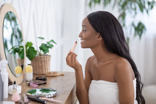 Hembra afroamericana se mira en el espejo y aplica lápiz labial desnudo en los labios — Foto de Stock