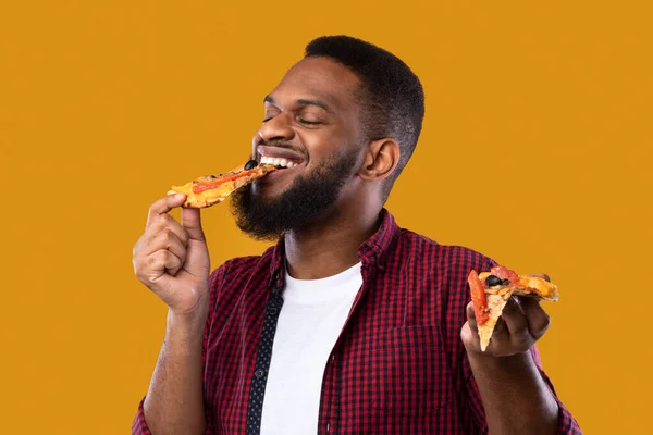 Preto cara comer pizza fatia com olhos fechados, fundo amarelo — Fotografia de Stock