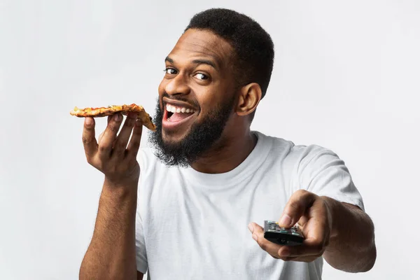 Alegre africano milenar homem comer pizza assistindo TV no estúdio — Fotografia de Stock