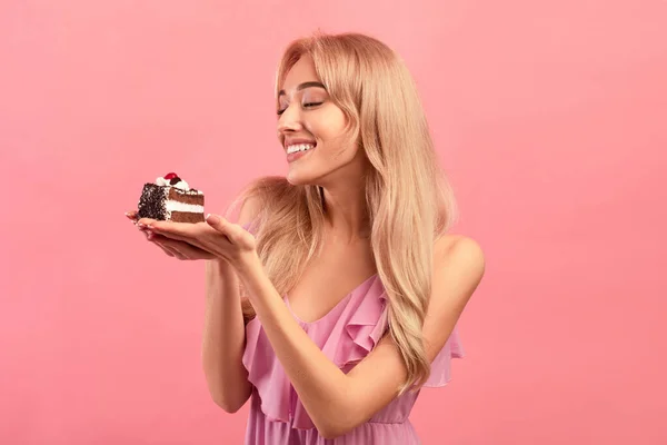 Encantadora dama caucásica sosteniendo delicioso pastel, disfrutando de su postre favorito en el cumpleaños, fondo de estudio rosa — Foto de Stock