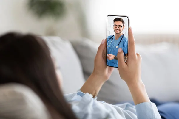 Donna sdraiata sul divano con smartphone avendo videoconferenza con medico terapista — Foto Stock