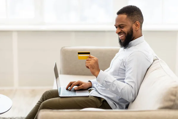 Hombre negro usando computadora y tarjeta de crédito de débito en casa — Foto de Stock