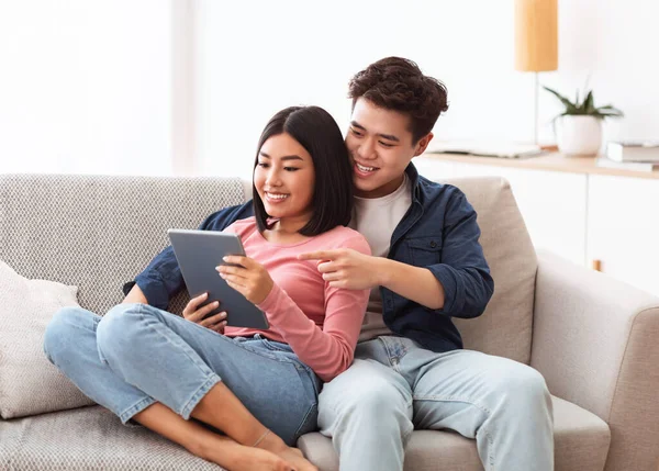 Cônjuges asiáticos felizes navegando na Internet no tablet digital em casa — Fotografia de Stock