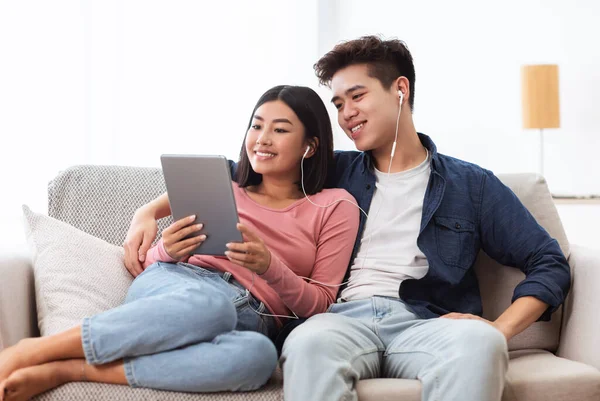 Casal coreano alegre usando o computador tablet digital sentado em casa — Fotografia de Stock