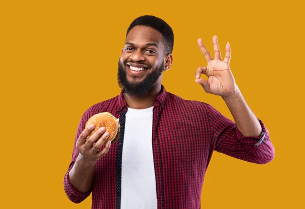 Africano cara posando com hambúrguer Gesturing Ok, Amarelo estúdio fundo — Fotografia de Stock