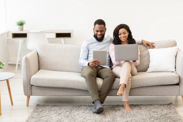 Africano casal americano sentado no sofá, usando laptop e tablet — Fotografia de Stock