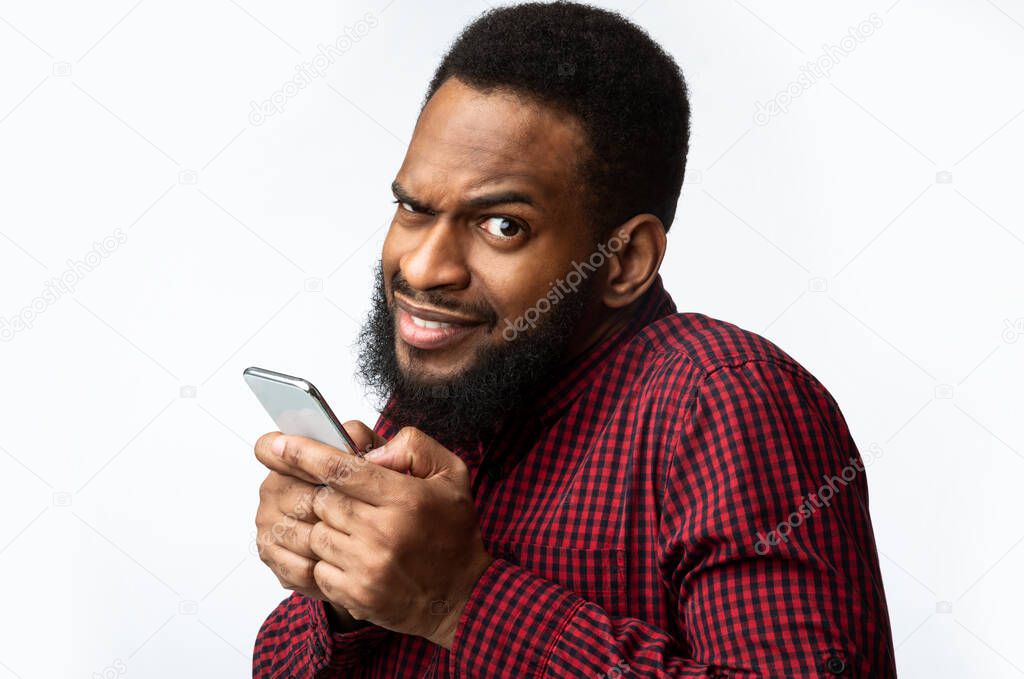 Suspicious Black Man Using Smartphone Looking At Camera, White Background.