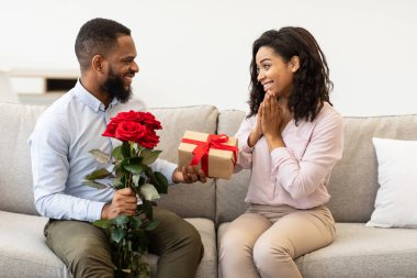 Genç siyah bir adam kırmızı güller ve kutuları kadınlara veriyor.