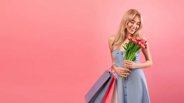 Nők napja. Bájos fiatal hölgy bevásárló táskák és tulipán virágok rózsaszín háttér, banner design copyspace — Stock Fotó