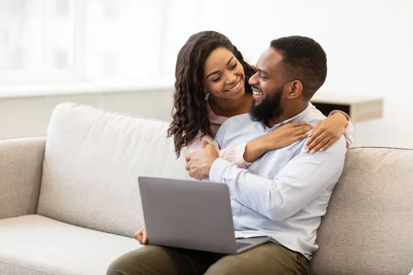 Afrikanisches Paar sitzt auf Couch, benutzt Laptop, kuschelt — Stockfoto