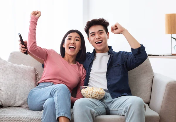 Emocionado casal chinês assistindo TV balançando punhos na sala de estar — Fotografia de Stock