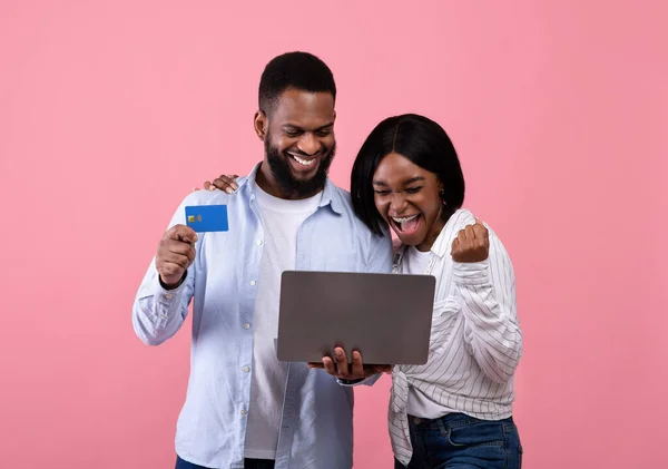 Heyecanlı siyah kadın ve erkek arkadaşı pembe arka planda kredi kartı ve laptopla online alışveriş yapıyorlar. — Stok fotoğraf