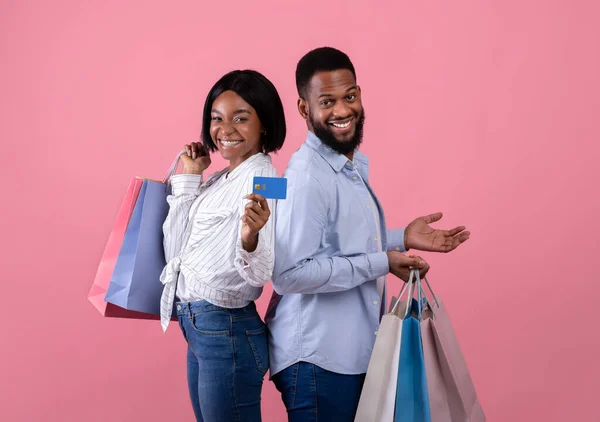 Retrato de familia milenaria negra sosteniendo bolsas de compras y tarjeta de crédito sobre fondo de estudio rosa —  Fotos de Stock