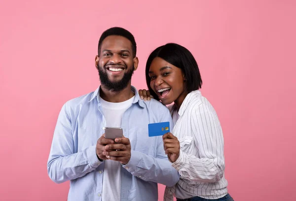 Pembe arka planda online alışveriş için akıllı telefon ve kredi kartı kullanan Afro-Amerikan çiftin portresi — Stok fotoğraf