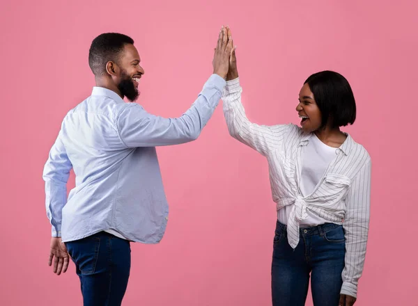 Teamwork and cooperation. Black couple giving high five to each other, celebrating common success on pink background — Stock Photo, Image