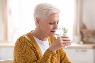 Güzel yaşlı bayan evde bir bardak su içiyor.