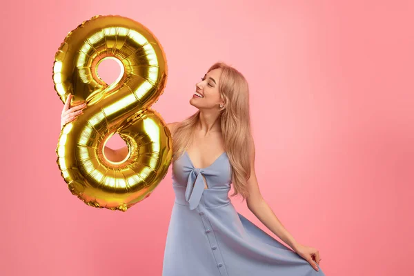 Celebración del 8 de marzo. Encantadora dama rubia sosteniendo el número ocho globo de oro para el Día de la Mujer sobre fondo rosa — Foto de Stock