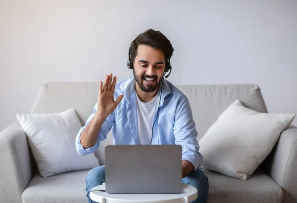 Amistoso hombre oriental haciendo videollamada con ordenador portátil y auriculares en casa —  Fotos de Stock