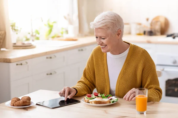 Smiling old lady using digital tablet while having lunch