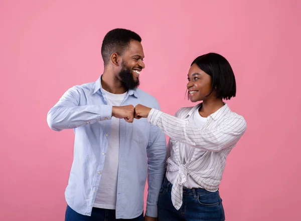 Cooperation, teamwork, partnership. Black couple making fist bump and looking at each other on pink background — Stock Photo, Image