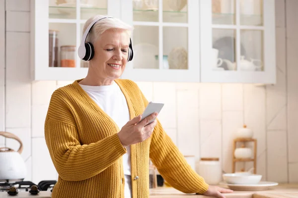 Mujer mayor feliz escuchando música en el teléfono inteligente en casa — Foto de Stock