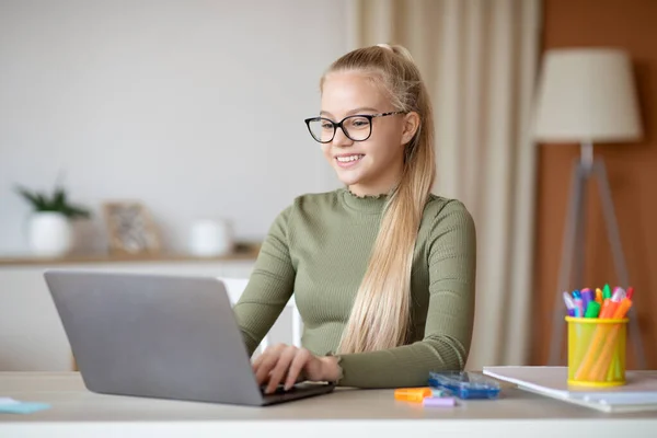 Весела дівчина-підліток сидить вдома, використовуючи ноутбук — стокове фото