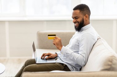 Siyah adam evde dizüstü bilgisayar ve banka kartı kullanıyor.