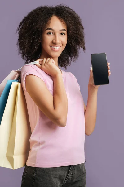 Sorridente millenaria afroamericana donna tiene molte borse della spesa a colori e mostra smartphone con schermo bianco — Foto Stock