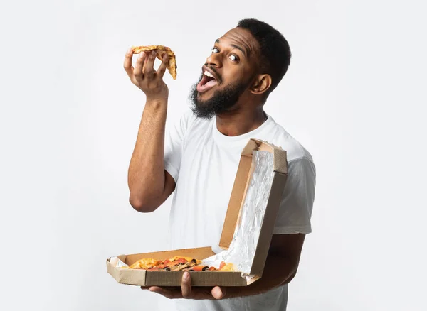 Cara preto comer pizza posando com grande caixa, fundo branco — Fotografia de Stock