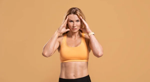 Triste donna di mezza età muscolosa in abbigliamento sportivo preme mani a testa soffre di mal di testa — Foto Stock