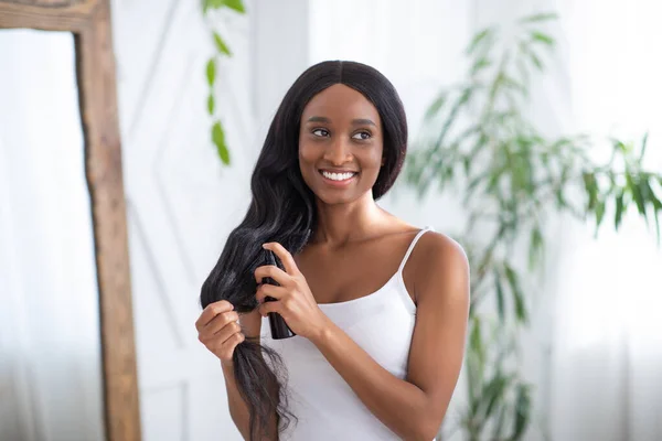 Hårvård kosmetika. Glad tusenårig afrikansk amerikansk kvinna tillämpa hårvård spray produkt på ändar — Stockfoto