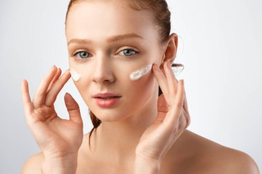 Kızıl saçlı genç bayan, Gri Arkaplan Üzerine Yüz Kremi Pozu Veriyor