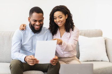 Gülümseyen afro çift evde belgeleri okuyor, anlaşmayı kontrol ediyor.