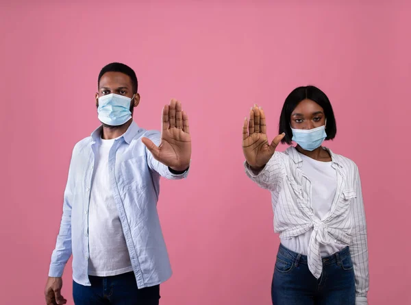 社会疏离和Covid-19大流行病。戴口罩的黑人夫妇在粉色背景上摆出STOP手势 — 图库照片