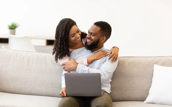 Feliz casal afro-americano sentado no sofá, usando laptop — Fotografia de Stock