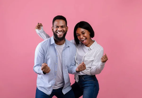 Fröhliche schwarze Ehepartner gestikulieren JA, schreien WOW, fühlen sich aufgeregt, feiern wichtige Errungenschaften auf rosa Hintergrund — Stockfoto