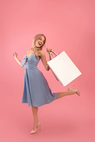 Весела молода жінка насолоджується покупками, несе подарункові пакети і бігає, щоб зберігати спеціальні пропозиції, рожевий фон — стокове фото