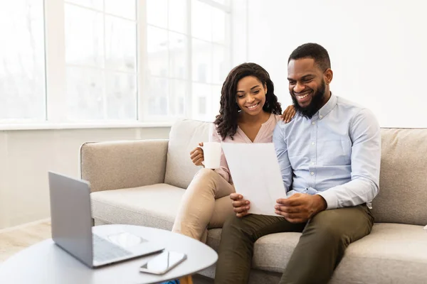 Positives schwarzes Paar liest Brief zu Hause, sitzt auf Couch — Stockfoto