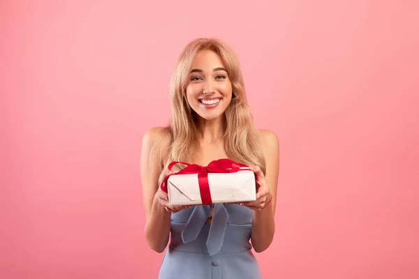 Bájos Y-generációs hölgy kezében ajándék doboz szalaggal, fogadó nők napja vagy születésnapi meglepetés rózsaszín háttér — Stock Fotó