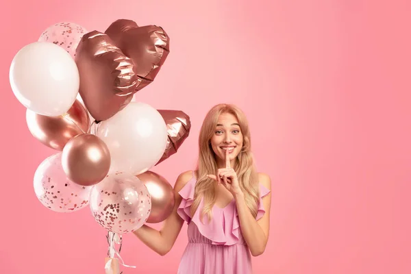 Stort salg eller tilbud om høytid. En lykkelig ung kvinne som holder ballonger og viser HUSH-tegn på rosa bakgrunn. – stockfoto