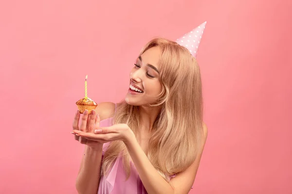 Vacker tusenårig kvinna i födelsedagshatt äta välsmakande tårta, firar B-dag på rosa bakgrund. Festligt koncept — Stockfoto