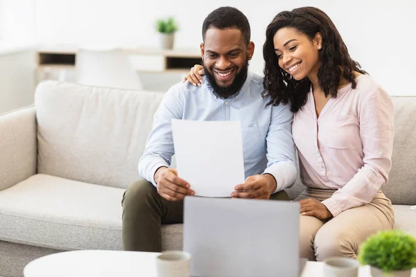 Positiva lettera di lettura di coppia nera a casa, seduta sul divano — Foto Stock