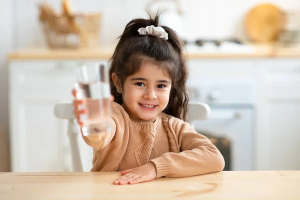 Sunn drikke. Søt, liten jente som holder glass med vann, sitter på kjøkkenet – stockfoto