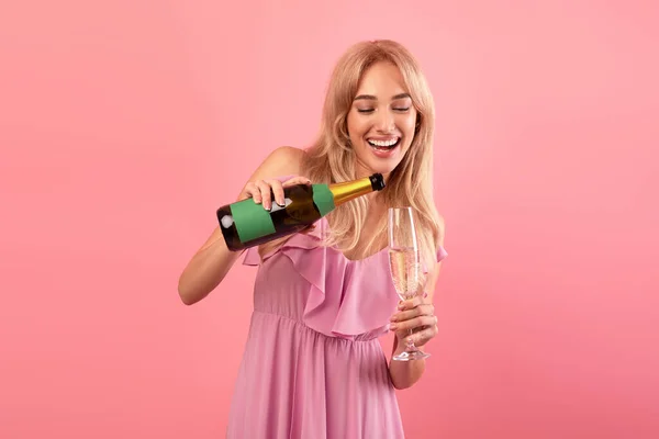 Senhora encantadora derramando vinho espumante de garrafa em vidro, celebrando férias, divertindo-se festa no fundo rosa — Fotografia de Stock